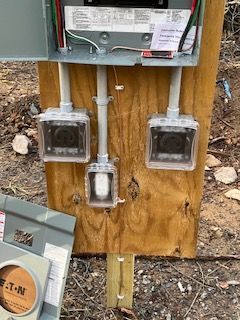 Electrical meter panel mounted on plywood with three clear-covered outlets and conduit pipes outdoors