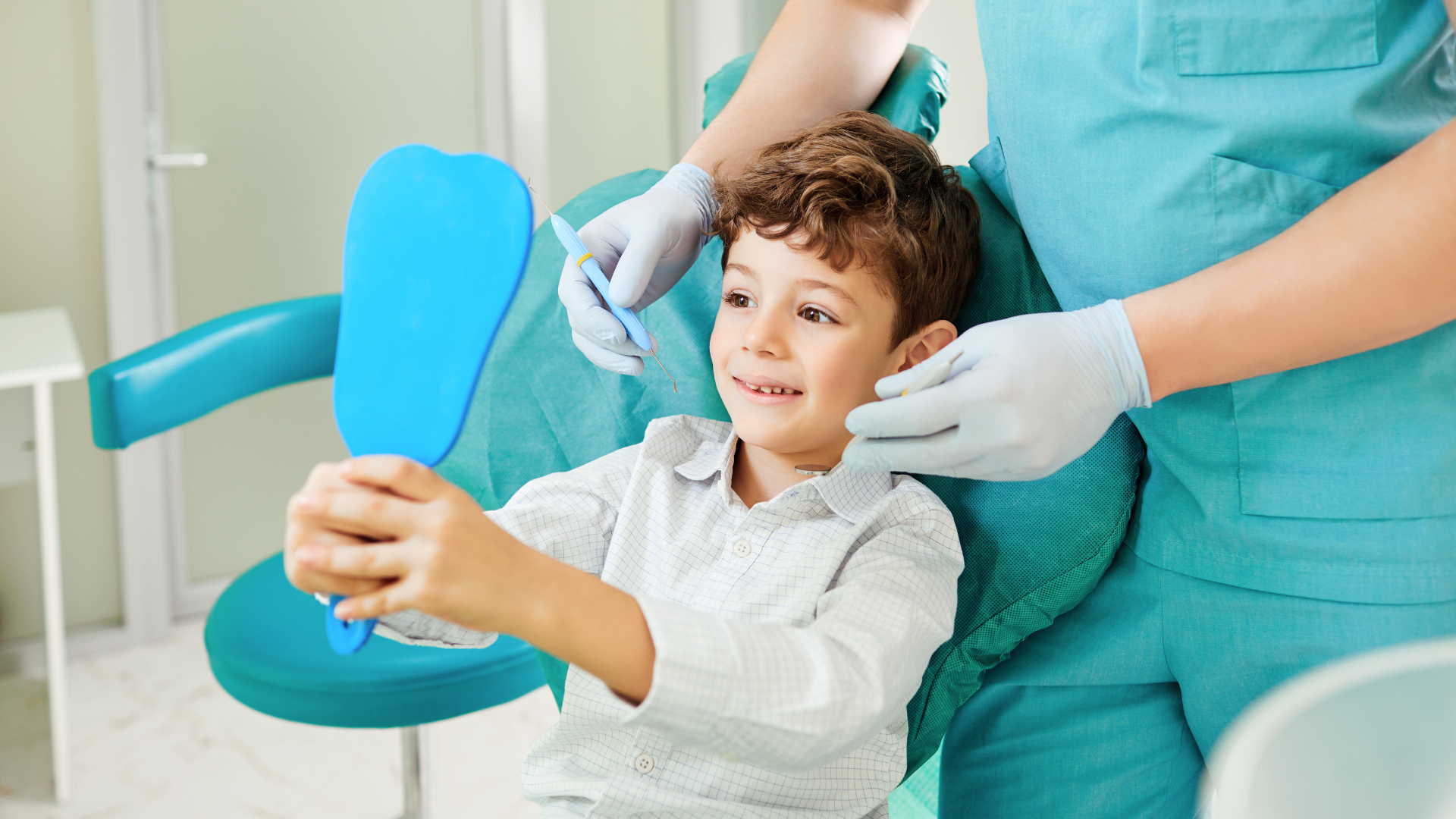 Child in a dental chair holding a blue mirror while a dentist in teal gloves checks their teeth