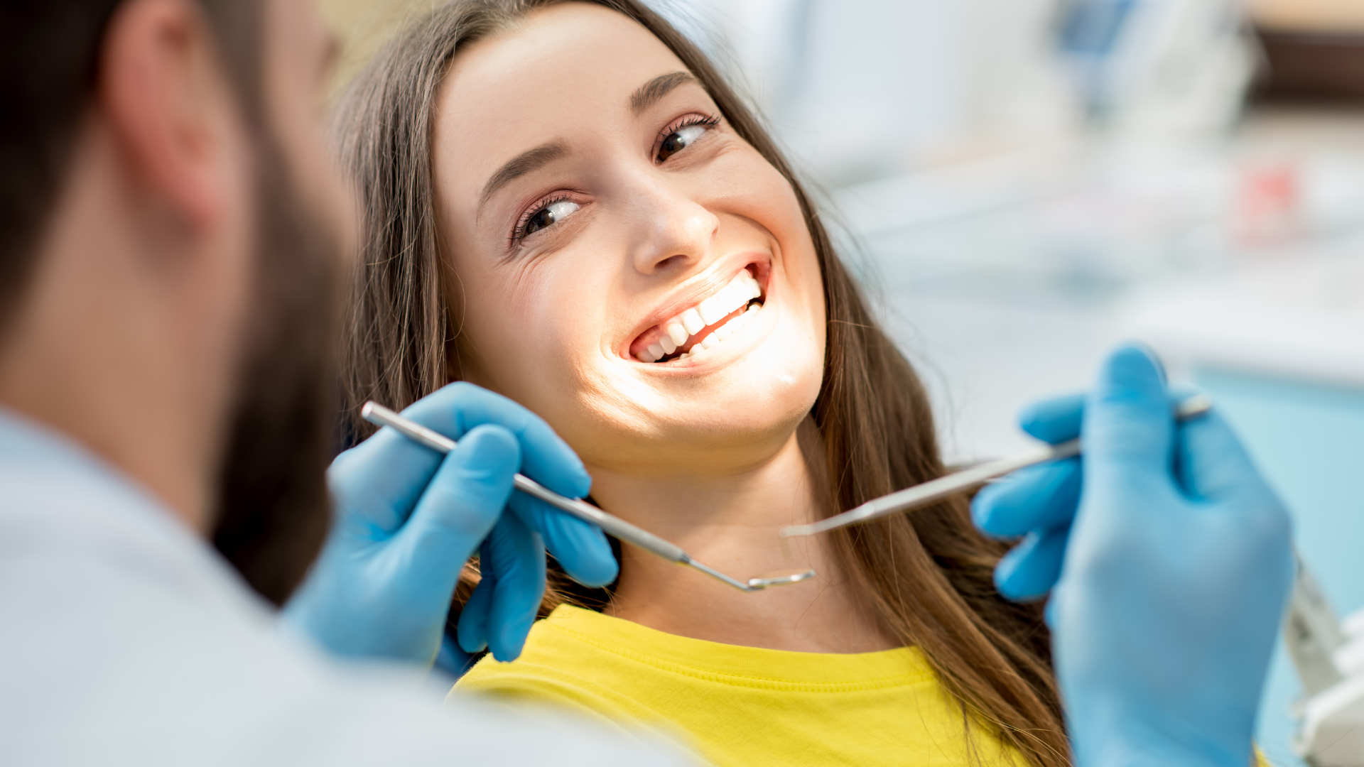 Dentist cleaning a smiling patient’s teeth with blue gloves and tools