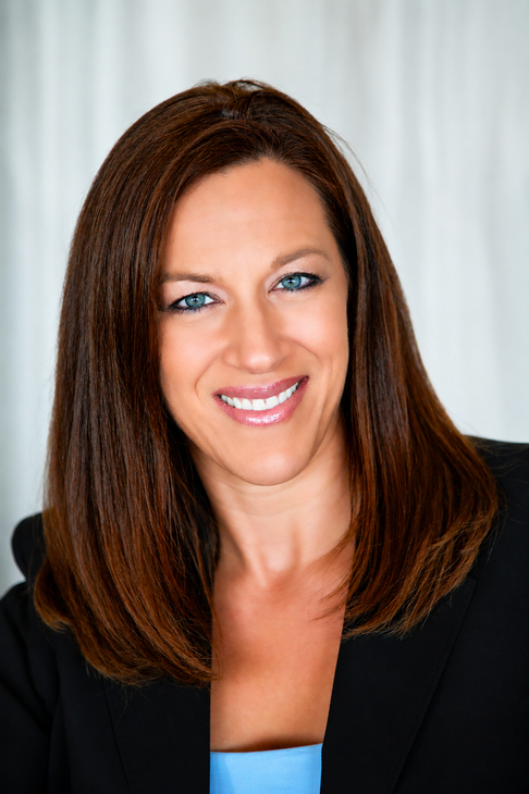 Smiling woman with long brown hair wearing a black blazer against a white background
