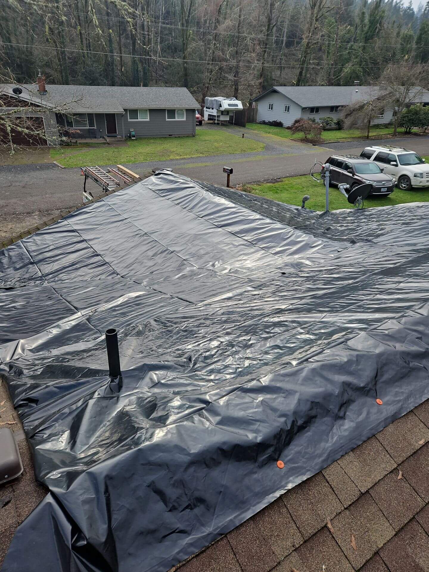 Roof covered with black tarp and shingles in a suburban neighborhood after storm damage