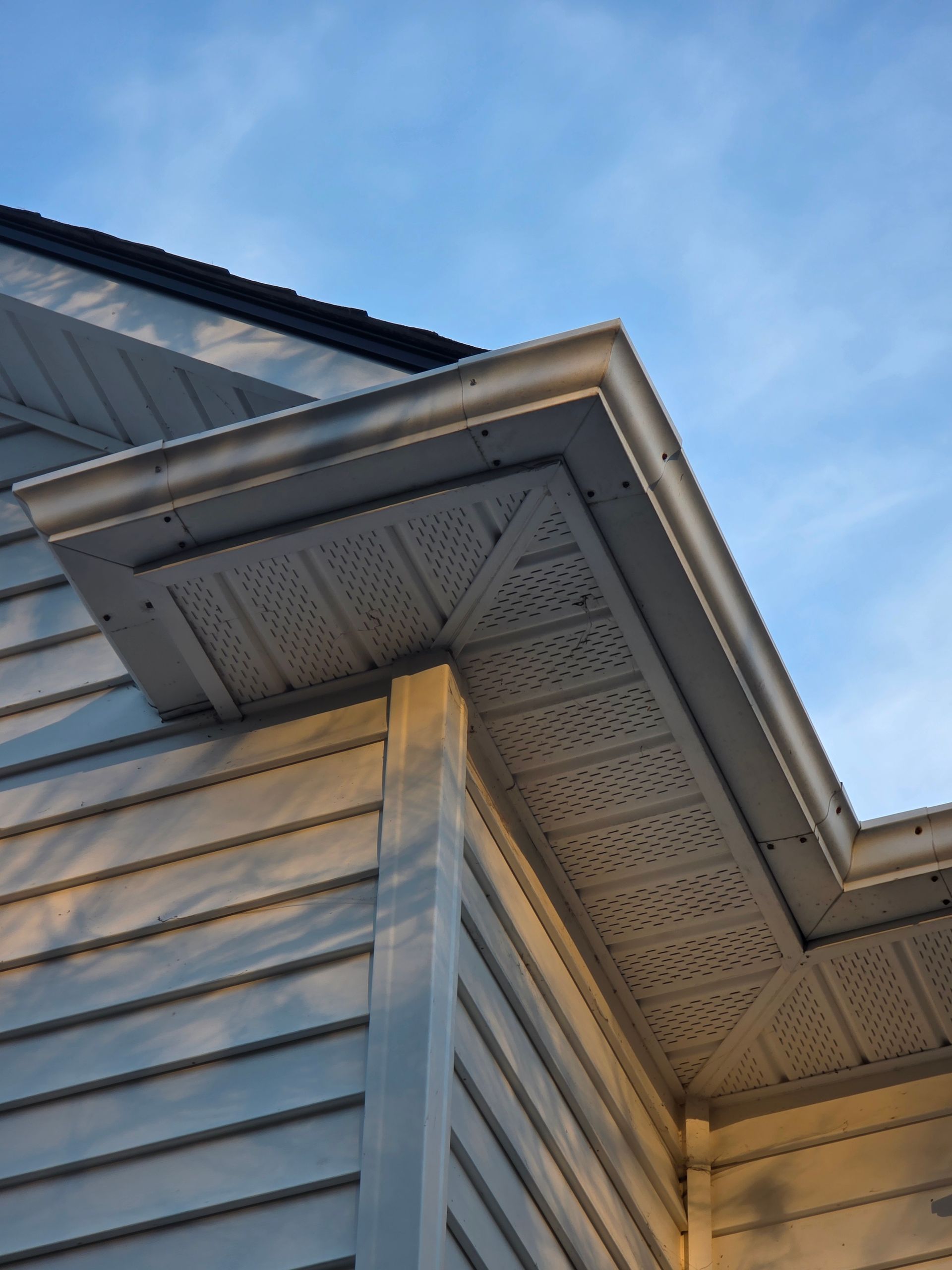 Low-angle view of the white soffit, fascia, and siding on the exterior corner of a house against a blue sky.