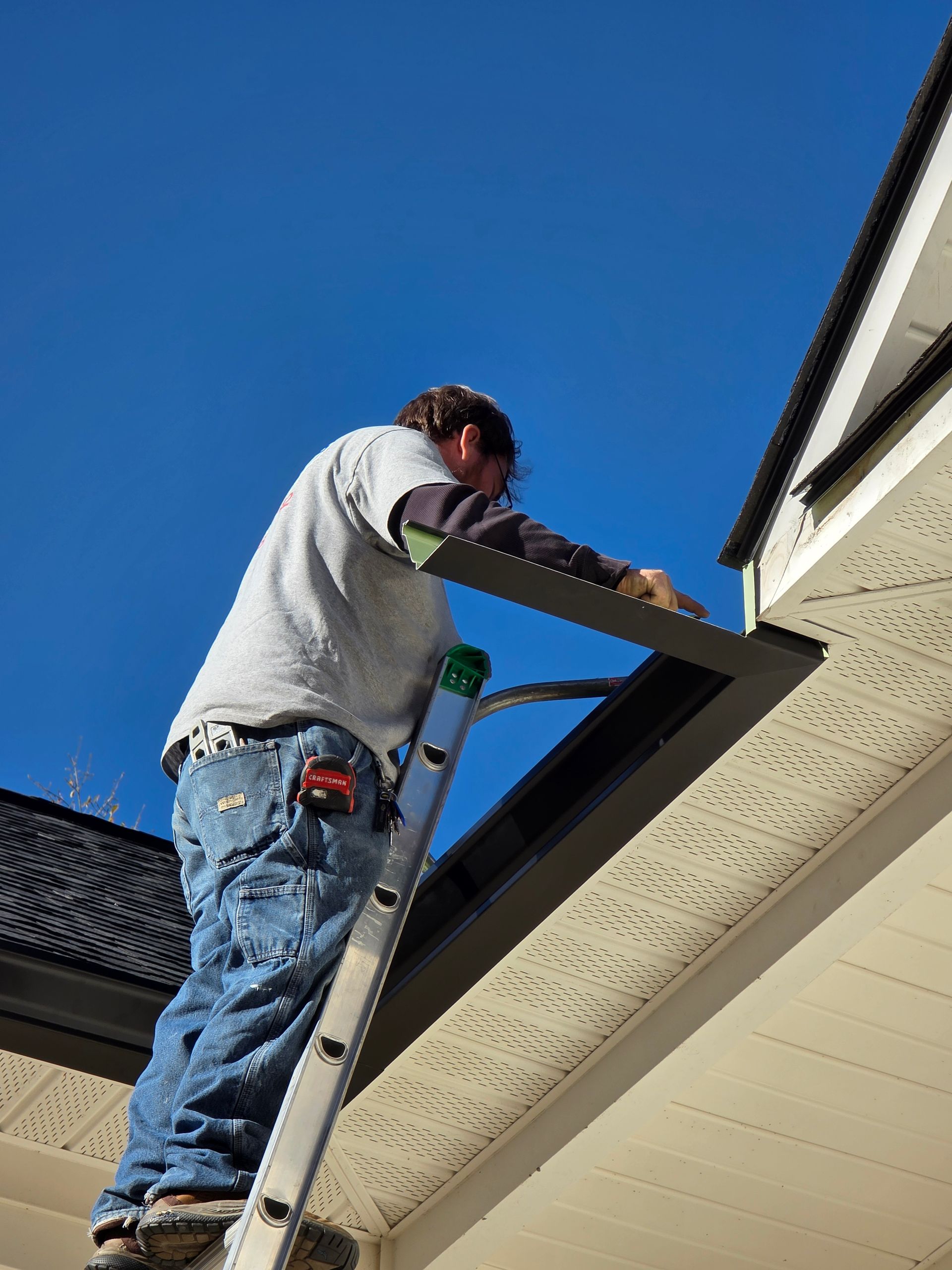 Worker on a ladder repairing the roof eaves beneath a blue sky