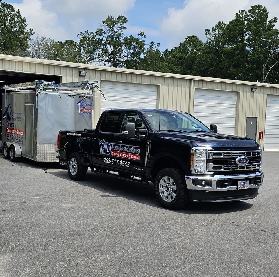 A black Ford pickup truck pulling a large silver utility trailer parked outside a metal warehouse building.