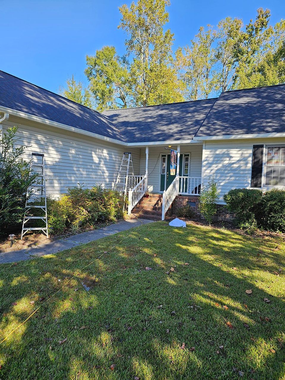 A single-story house with a white exterior, dark roof, and a front porch, featuring a ladder leaning against the wall.