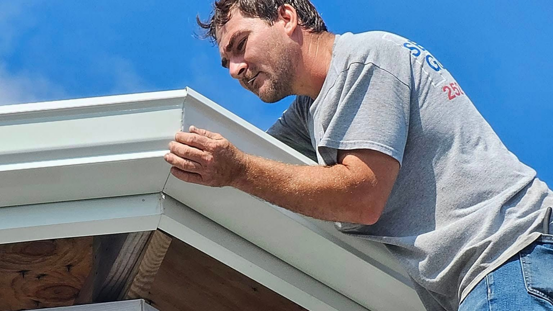 Worker installing white roof trim on a house eave under a blue sky