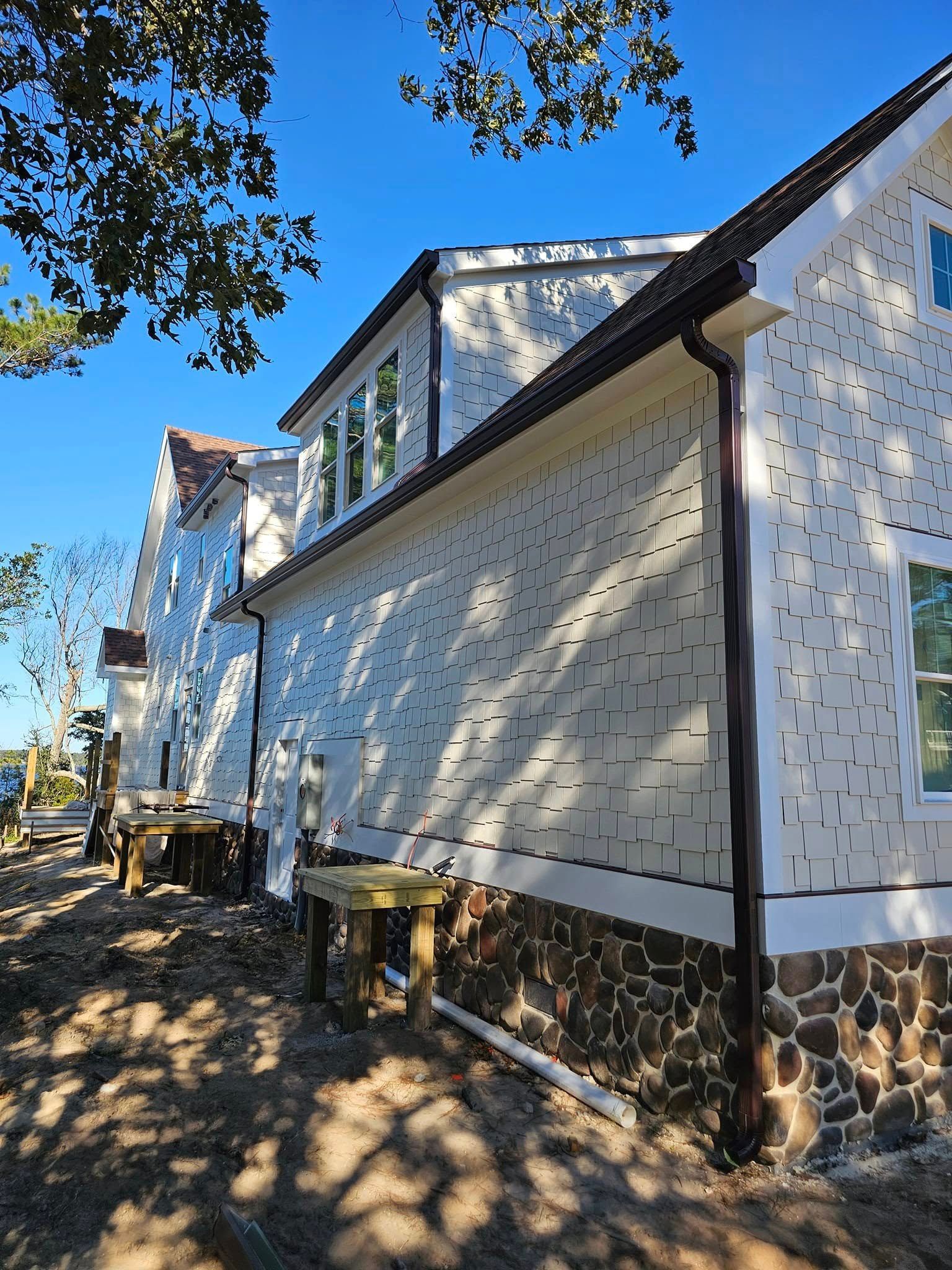 A modern house with a white stucco facade featuring a decorative grid pattern, stone base, and dark trim under a blue sky.