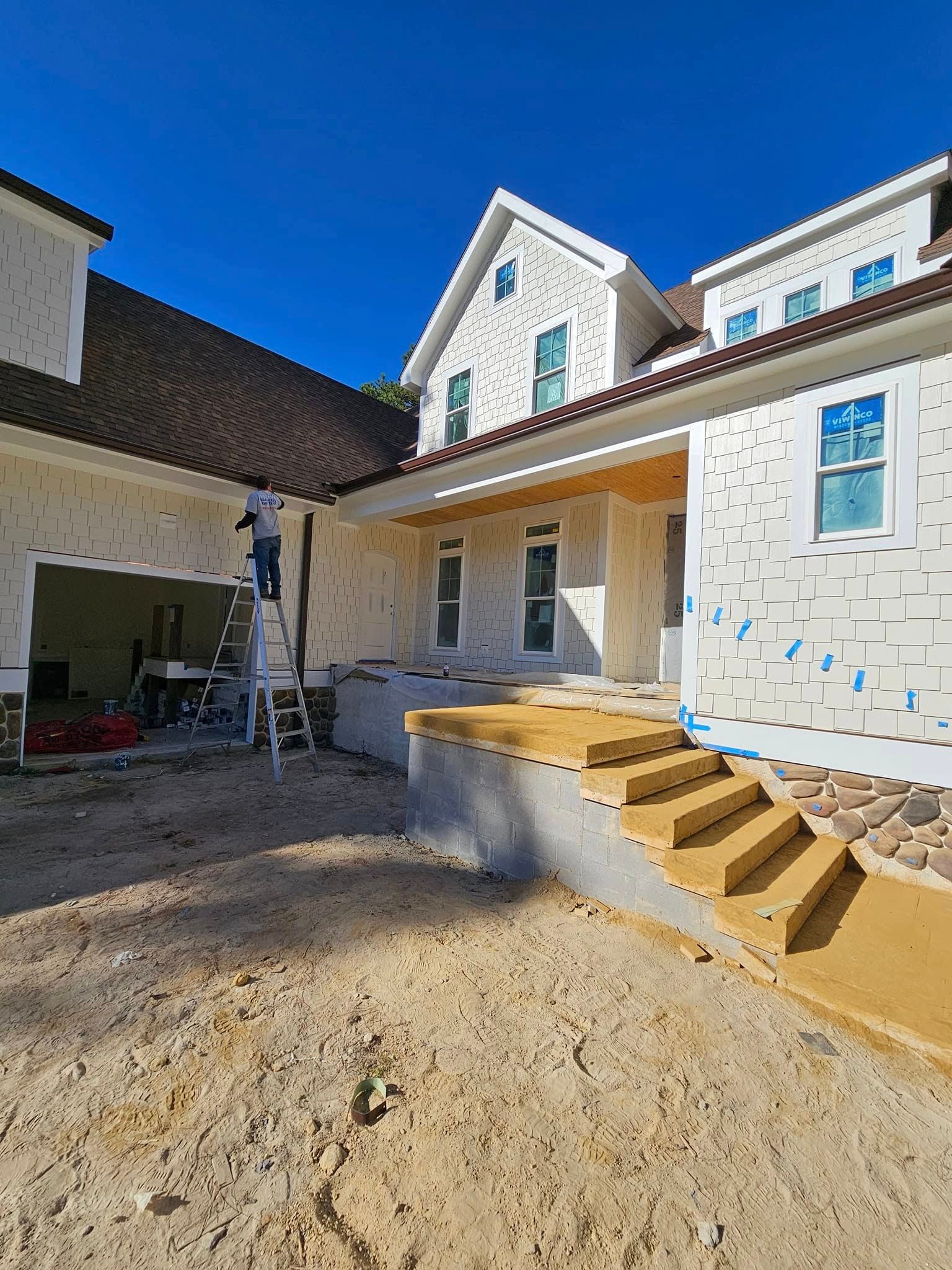 A worker on a ladder installs white exterior foam insulation on a residential building under a bright blue sky.