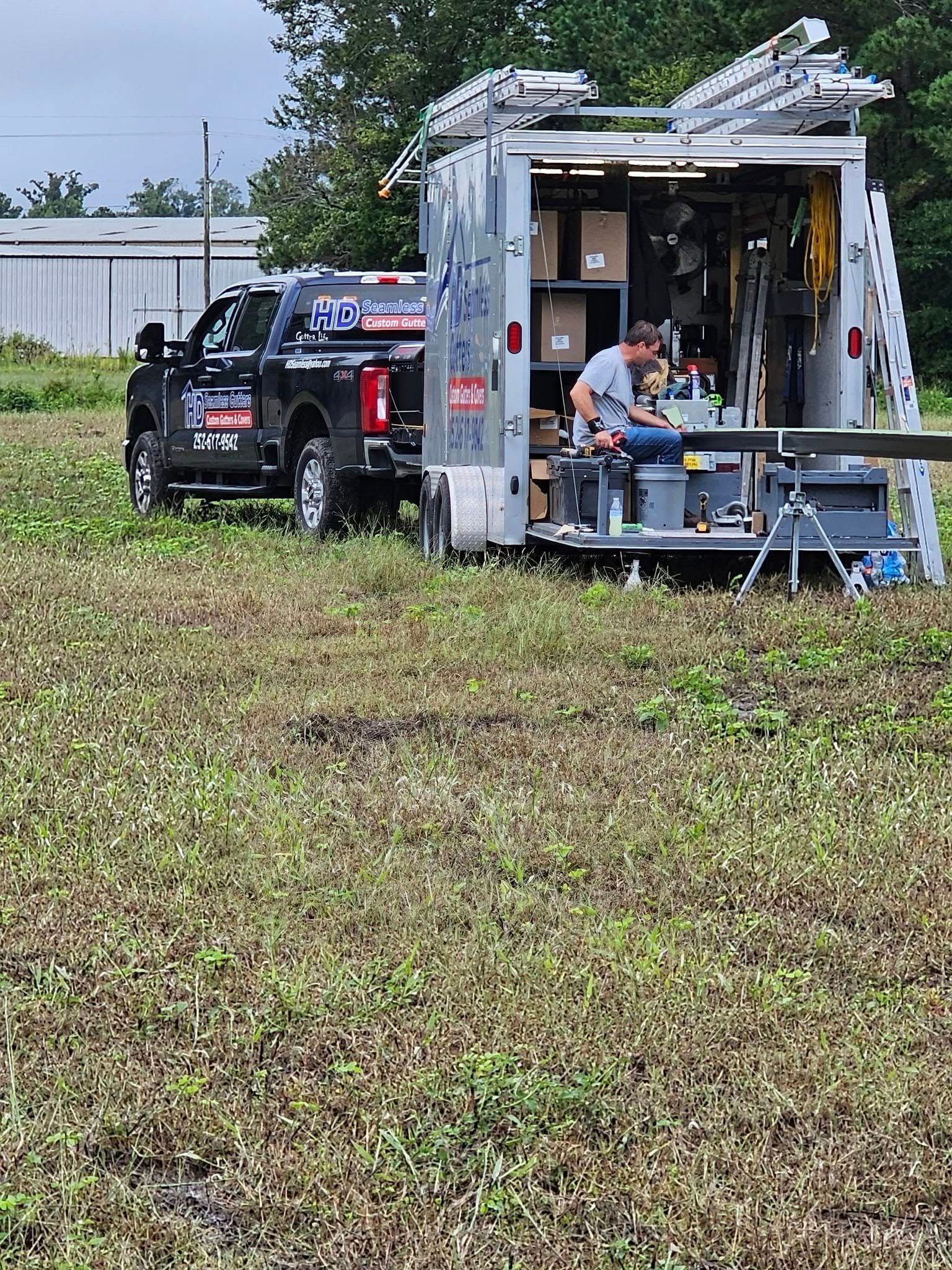 A person sits inside a utility trailer parked in a field, working at a station with a laptop and equipment.