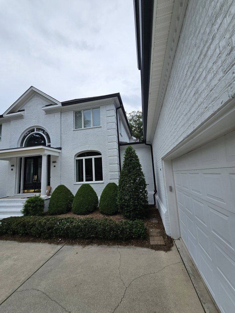 A two-story white brick house with black accents, a front entrance, a garage, and landscaped evergreen shrubs.