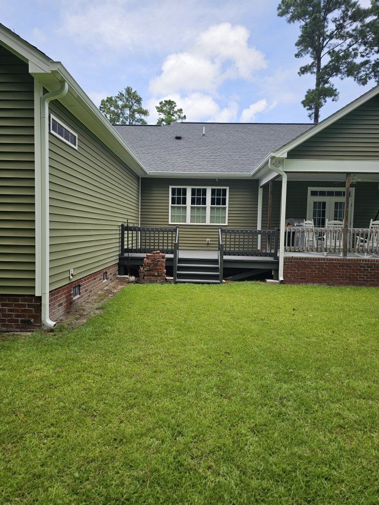 Green house exterior with a dark wooden deck and stairs connecting two sections of the building above a brick foundation.
