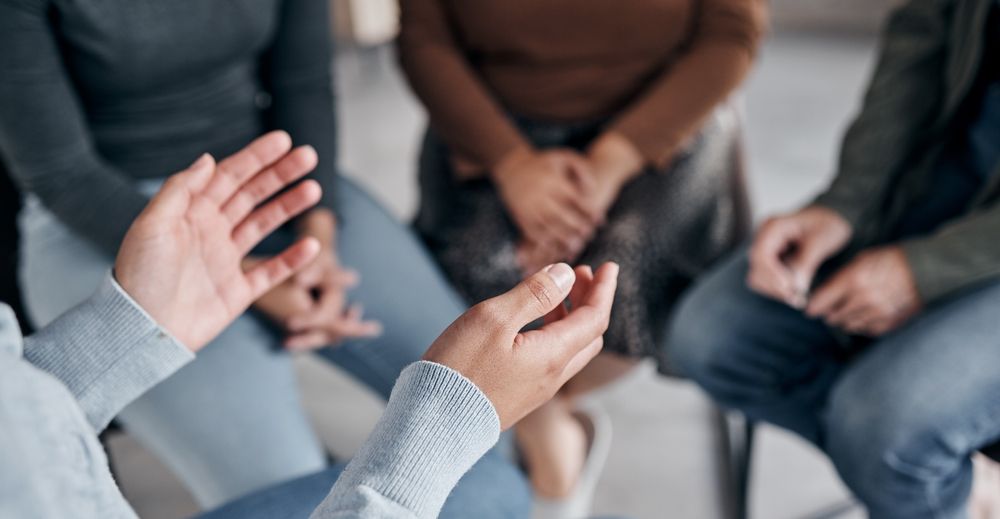 Hands gesturing towards a seated group in a circle, likely a therapy session.