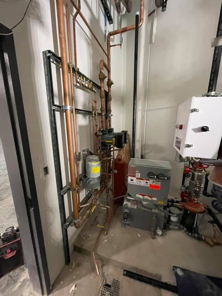 Industrial mechanical room with pipes, valves, pumps, and electrical equipment along a narrow hallway.