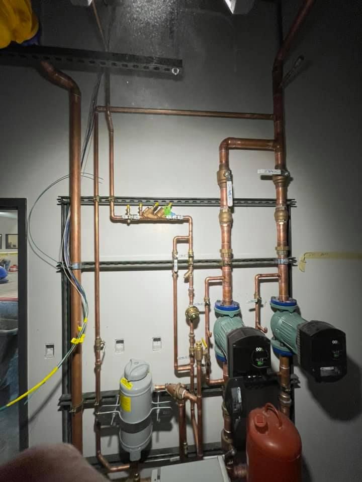 Mechanical room with copper pipes, pumps, and water tanks against a gray wall