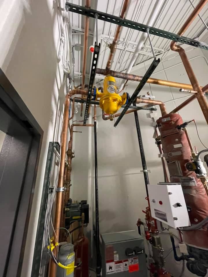 Industrial ceiling area with pipes and valves, including a yellow overhead hoist in a mechanical room
