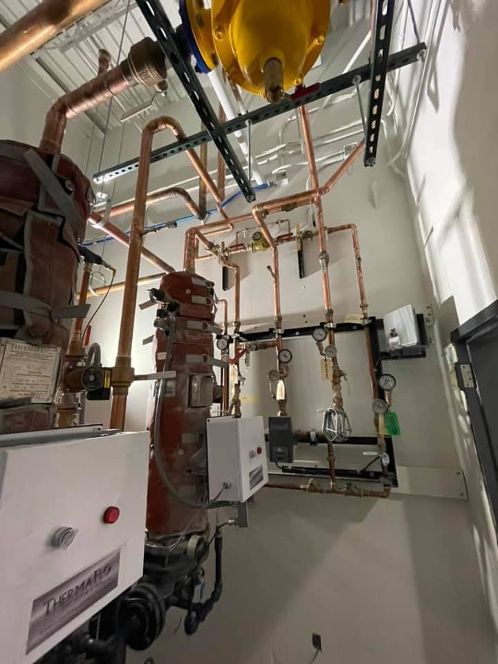 Mechanical room with pipes, valves, and wall-mounted equipment in a narrow utility space