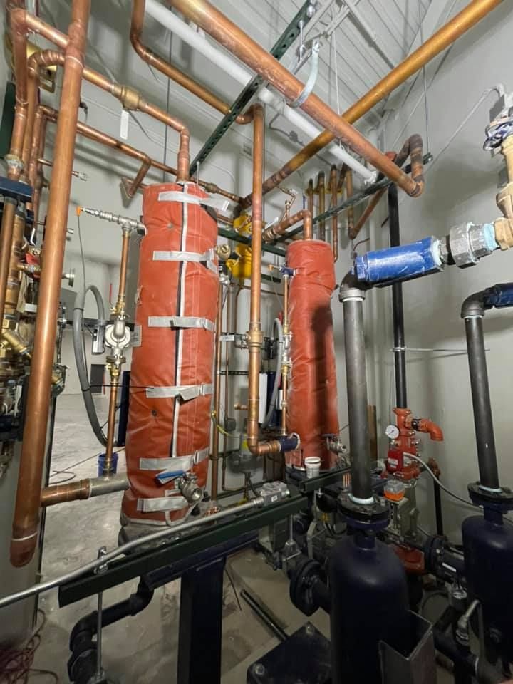 Industrial mechanical room with red insulated pipes, black valves, and copper piping overhead