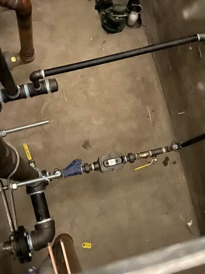 Underfloor plumbing with black pipes, valves, and fittings on a concrete floor. Underfloor plumbing with black pipes, valves, and fittings on a concrete floor.
