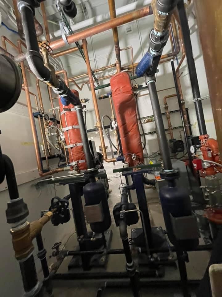 Industrial mechanical room with copper pipes, insulated ducts, and black pumps on a concrete floor Industrial mechanical room with copper pipes, insulated ducts, and black pumps on a concrete floor