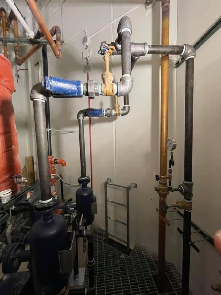 Industrial piping and valves in a mechanical room, with blue and orange insulated pipes and a metal floor grate. Industrial piping and valves in a mechanical room, with blue and orange insulated pipes and a metal floor grate.