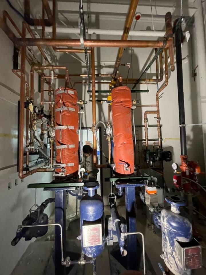 Boiler room with orange insulated pipes, valves, and pumps in a mechanical utility space Boiler room with orange insulated pipes, valves, and pumps in a mechanical utility space
