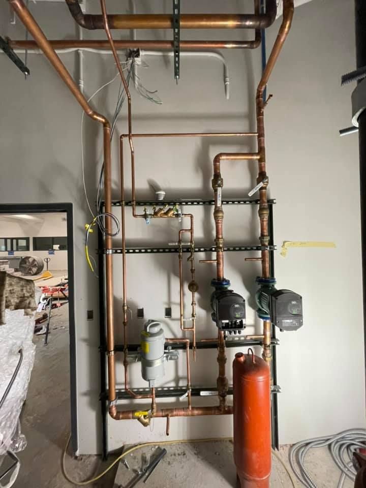 Copper plumbing and valves on a wall, with a red tank in an unfinished utility room.