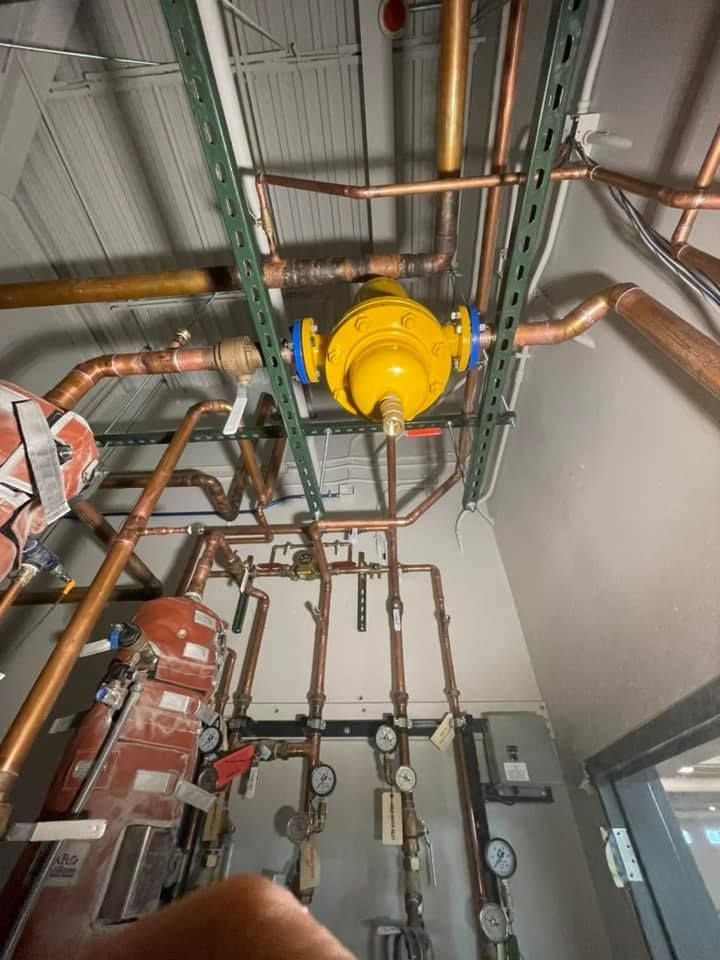 Ceiling pipes and valves in an industrial utility room, with a yellow valve assembly and gauges.
