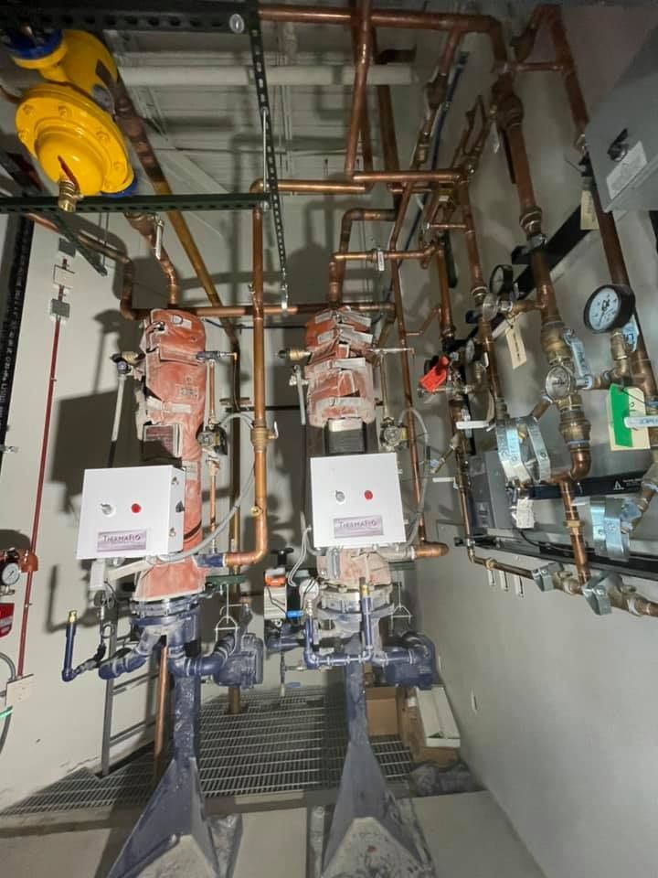 Industrial utility room with pipes, valves, gauges, and two wall-mounted machines in a narrow service area
