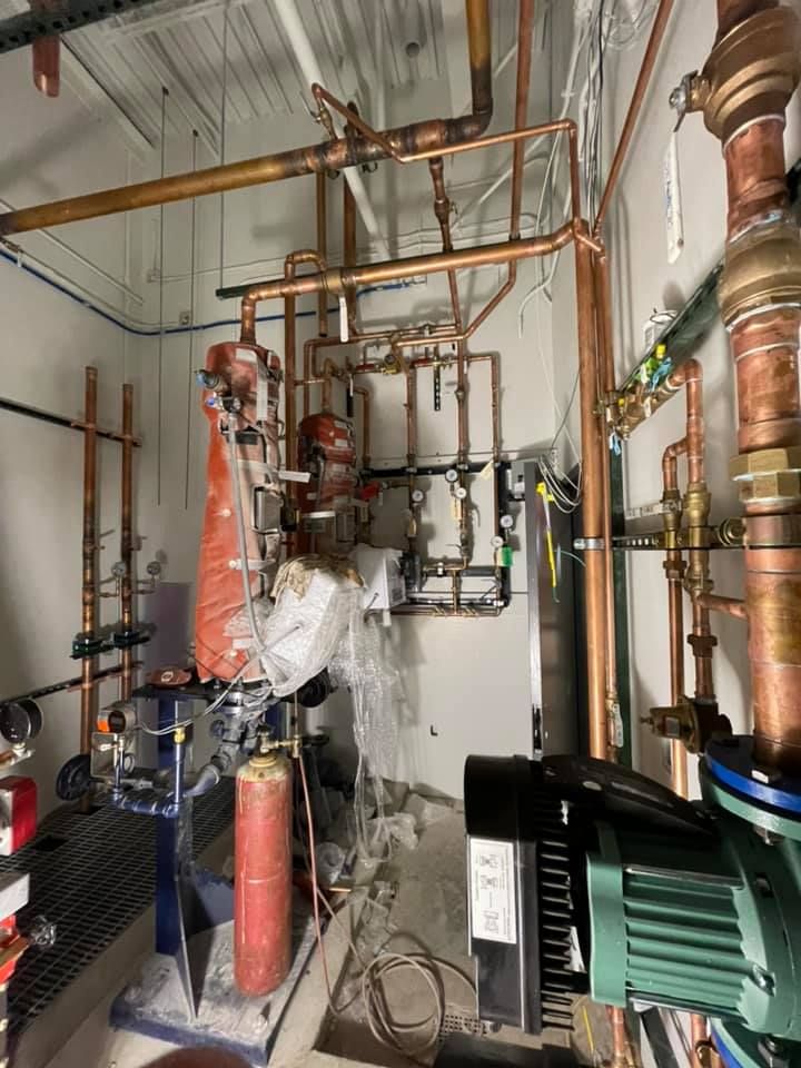 Copper plumbing and a green pump in a mechanical room with pipes, valves, and insulation.