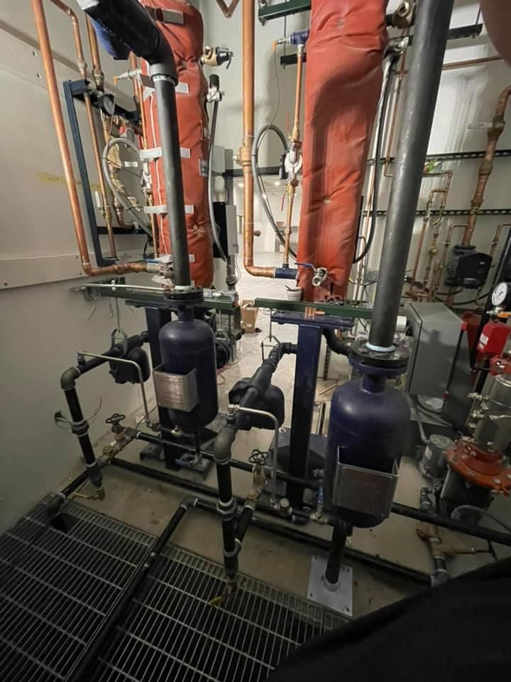 Industrial piping with two black pumps and orange insulated ducts in a mechanical room