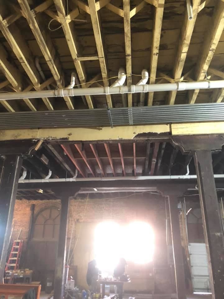 Interior of a wooden building under renovation, with exposed beams and bright sunlight streaming through the back entrance. Interior of a wooden building under renovation, with exposed beams and bright sunlight streaming through the back entrance.