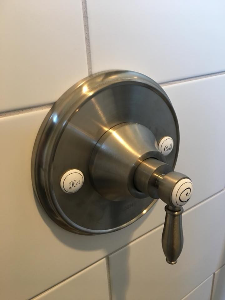 Brushed metal shower knob on white tiled wall with a small lever handle