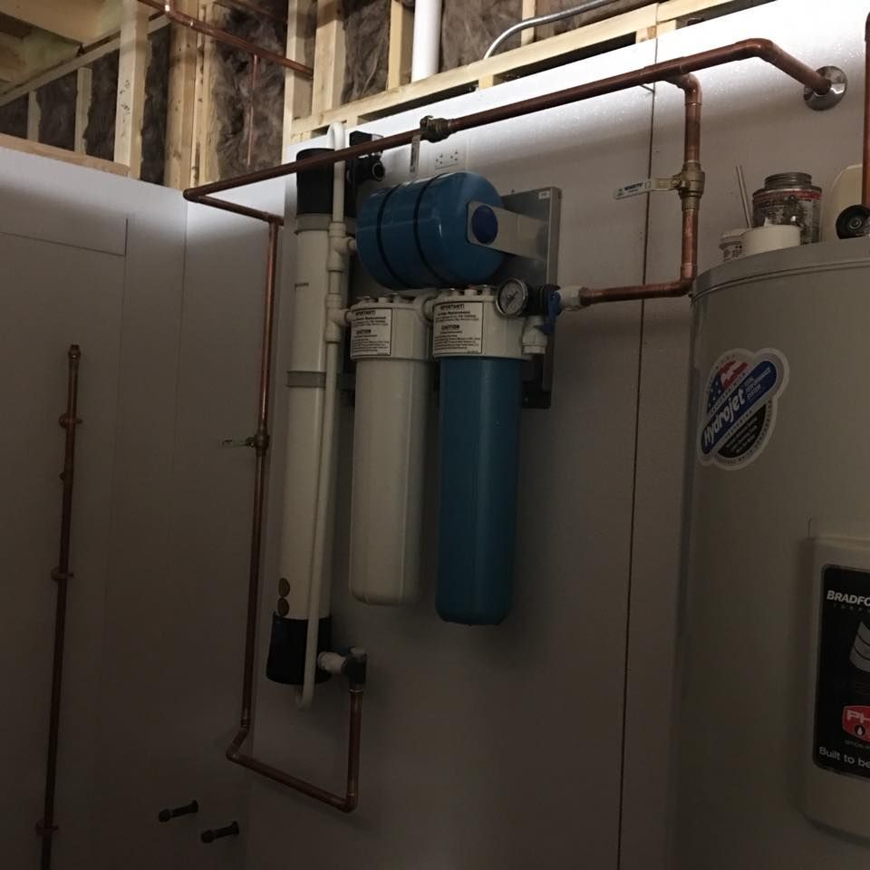 Blue water treatment tanks and copper pipes installed in a utility room. Blue water treatment tanks and copper pipes installed in a utility room.