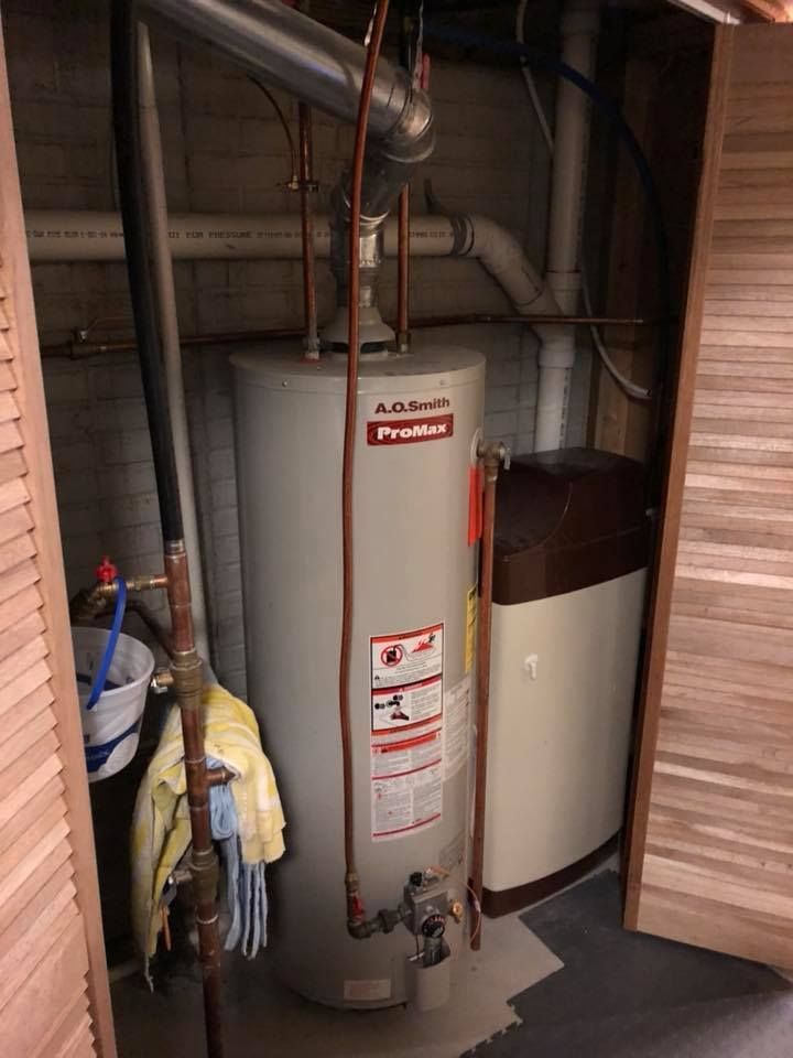 Water heater and furnace in a narrow utility closet with exposed pipes and hanging coats. Water heater and furnace in a narrow utility closet with exposed pipes and hanging coats.