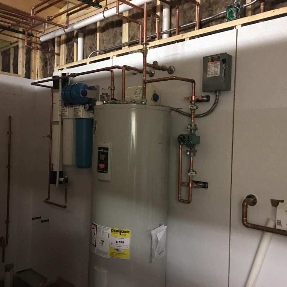 Utility room with a large white water heater, pipes, valves, and wall-mounted controls. Utility room with a large white water heater, pipes, valves, and wall-mounted controls.