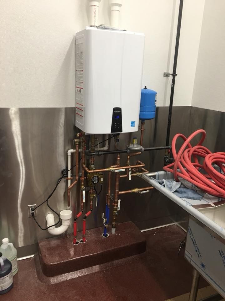 Wall-mounted white water heater with exposed pipes and red hoses in a utility room