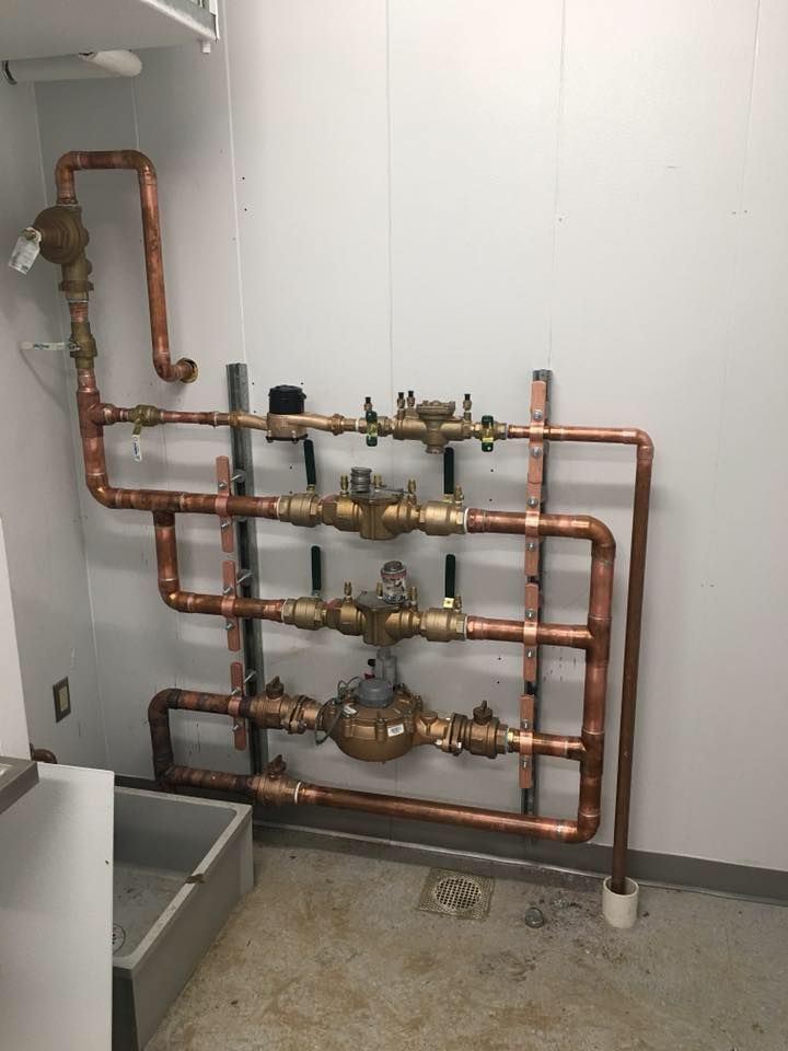 Indoor plumbing pipes and valves mounted on a wall above a gray utility basin.