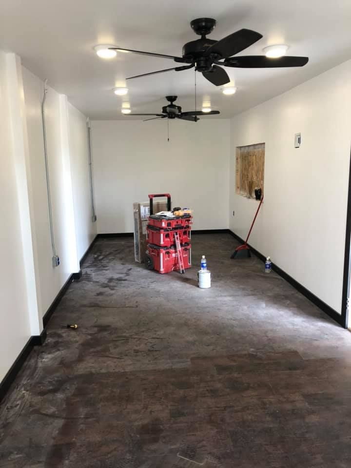 Empty long room with white walls, dark carpet, ceiling fans, and a red tool cart near the back wall