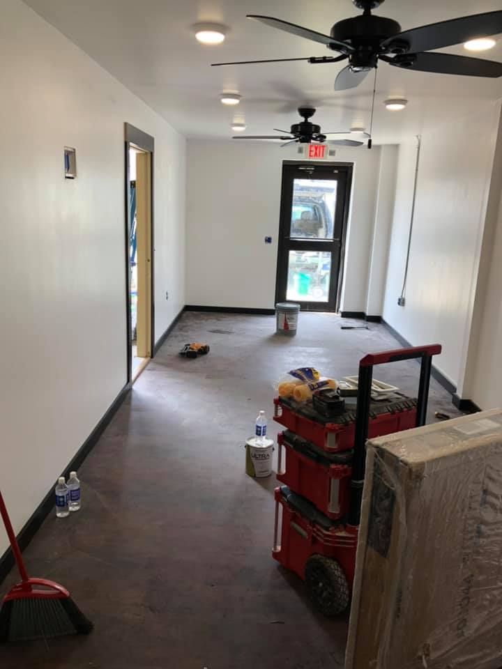 Empty hallway under renovation with red cleaning equipment, white walls, and ceiling fans.