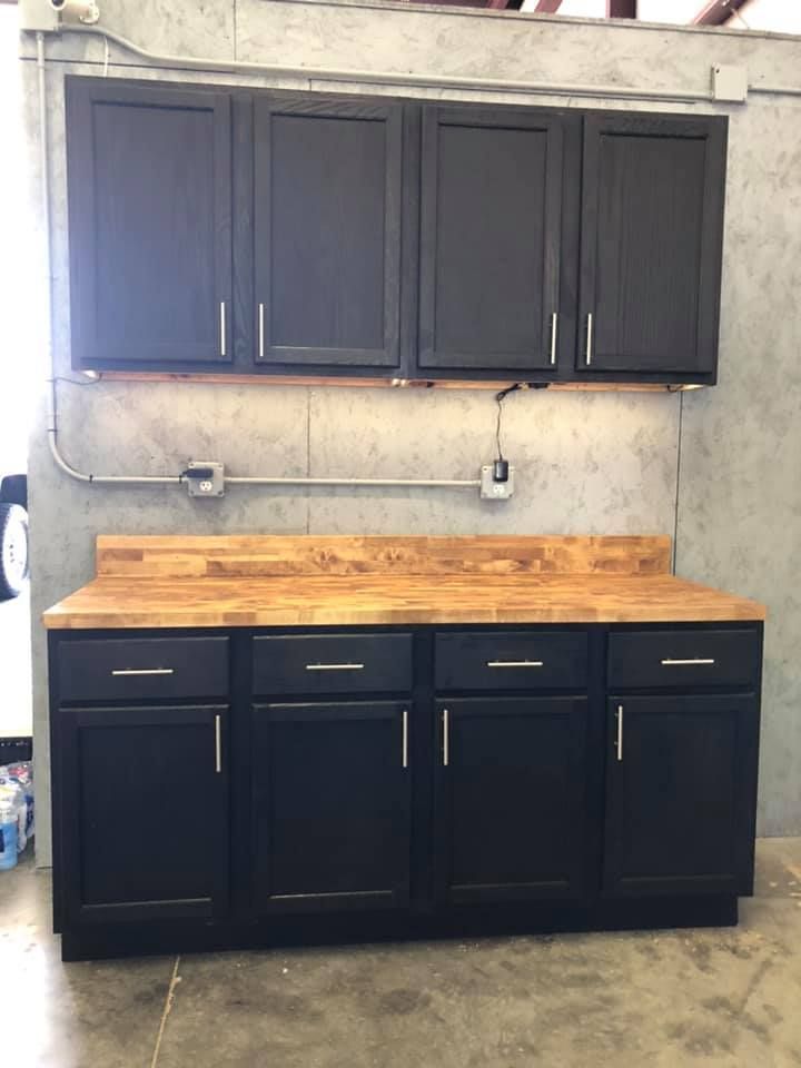 Black wall cabinets above a wood workbench with black base cabinets in a garage or workshop Black wall cabinets above a wood workbench with black base cabinets in a garage or workshop