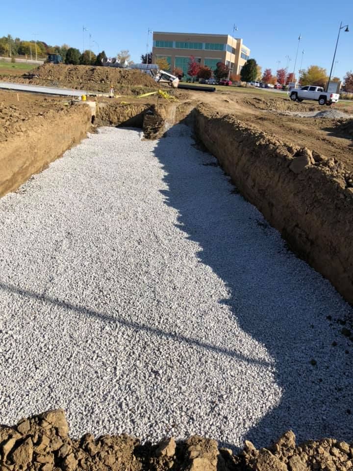 Gravel-filled trench at a construction site with a building in the distance