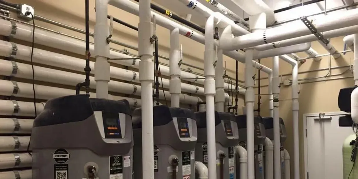 Basement mechanical room with large gray HVAC units and rows of white pipes overhead