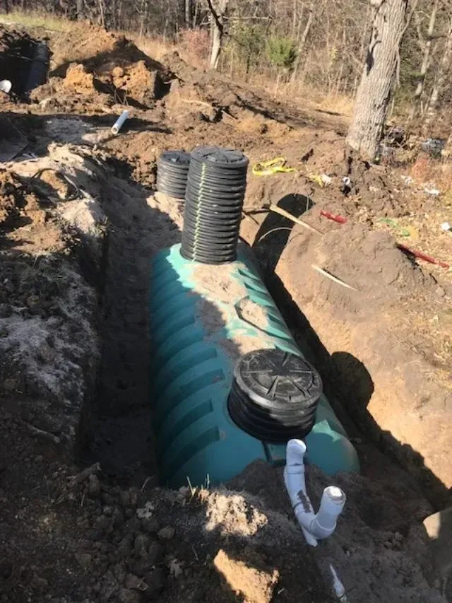 Underground septic tank installation with black vent pipes and white plumbing in a dirt trench