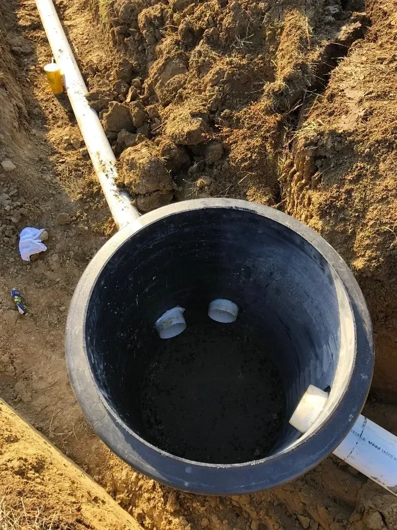 Black utility pipe opening in a dirt trench with white PVC pipes entering from the sides.