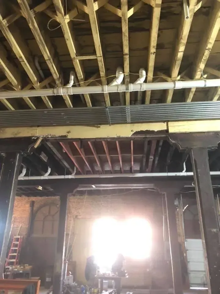 Dim unfinished interior with exposed beams, tall posts, and bright light through an open doorway.