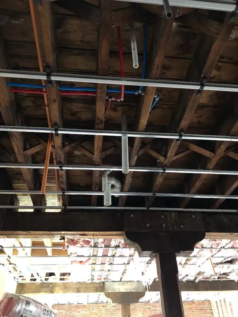 Exposed wooden ceiling beams with metal pipes and conduits in an unfinished interior. Exposed wooden ceiling beams with metal pipes and conduits in an unfinished interior.