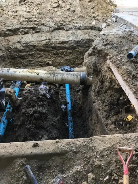Excavation trench with exposed blue pipes and a corrugated pipe across muddy soil. Excavation trench with exposed blue pipes and a corrugated pipe across muddy soil.