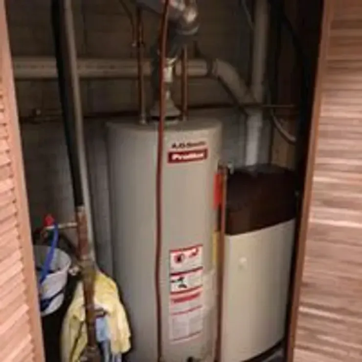 Utility closet with a water heater, furnace, and cleaning supplies in a cramped basement space