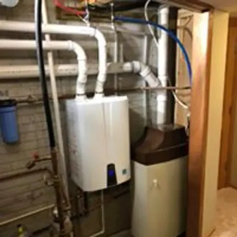 Basement utility area with a white water heater, pipes, and a beige storage tank. Basement utility area with a white water heater, pipes, and a beige storage tank.