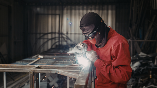 Worker in red jacket welding metal in an industrial workshop, bright sparks flying.